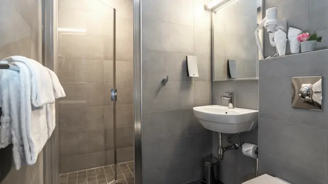 Bad med dusj, grå fliser og servant.