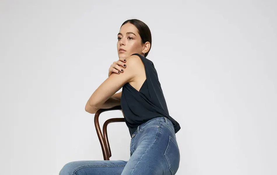 kvinnelig modell som sitter på stol, viser frem svart singlet, jeans og svarte, høye hæler