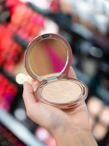 Nærbilde av en hånd som holder et åpent pudder med speil