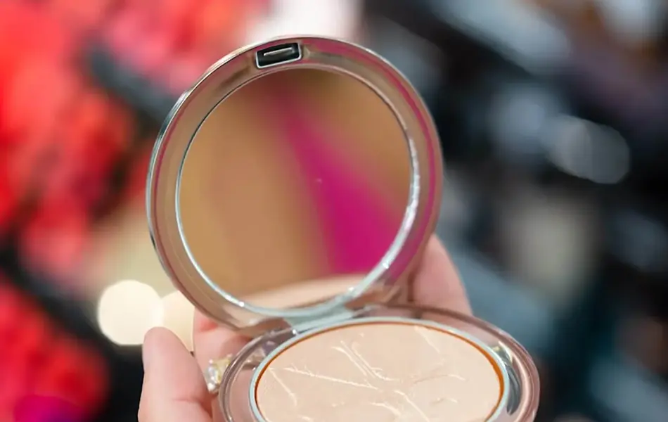 Nærbilde av en hånd som holder et åpent pudder med speil