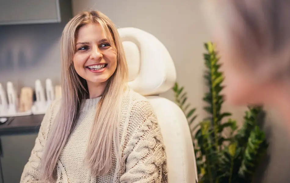 Jente sitter i en behandlingsstol og smiler