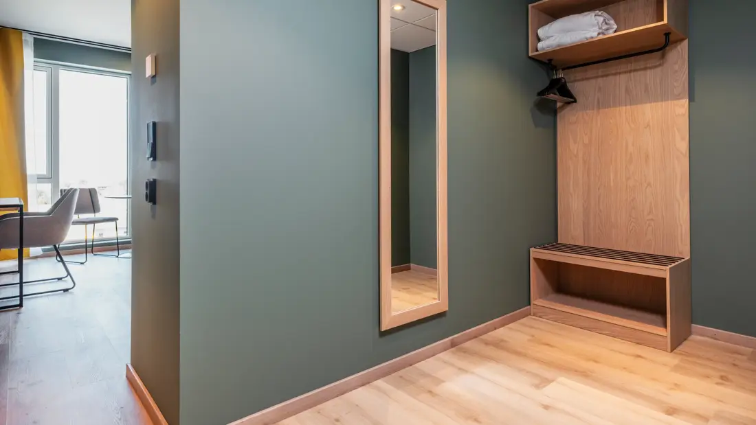 Inngangsparti i superior rom med garderobe, helspeil, grønne vegger og parkett.