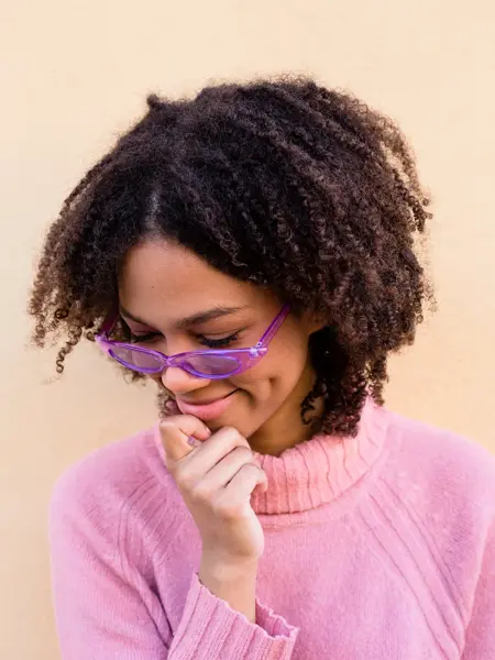 Nærbilde av dame med pastellrosa genser og lilla, transparente solbriller