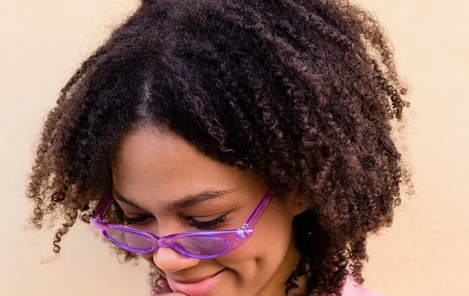 Nærbilde av dame med pastellrosa genser og lilla, transparente solbriller