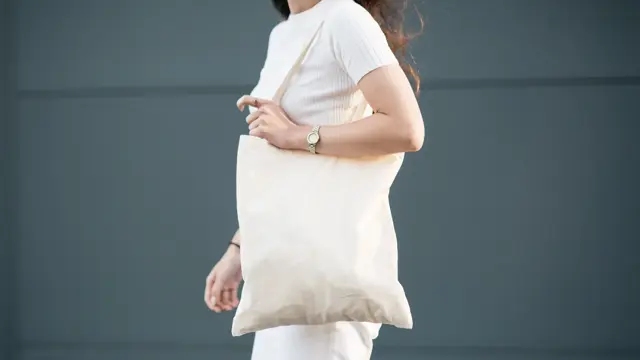 Halvportrett av dame med hvit t-skjorte, hvit totebag og hvit bukse 