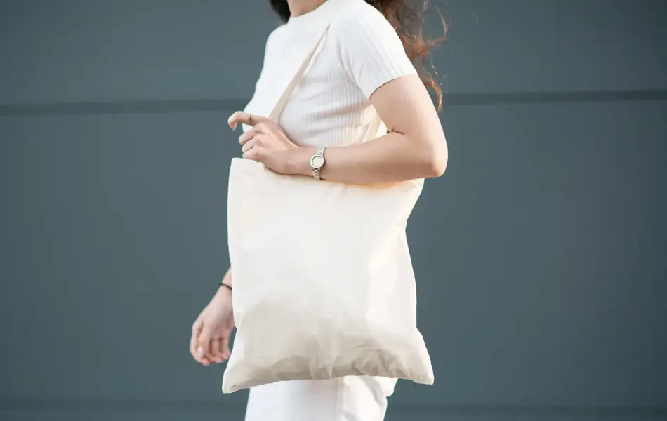 Halvportrett av dame med hvit t-skjorte, hvit totebag og hvit bukse 