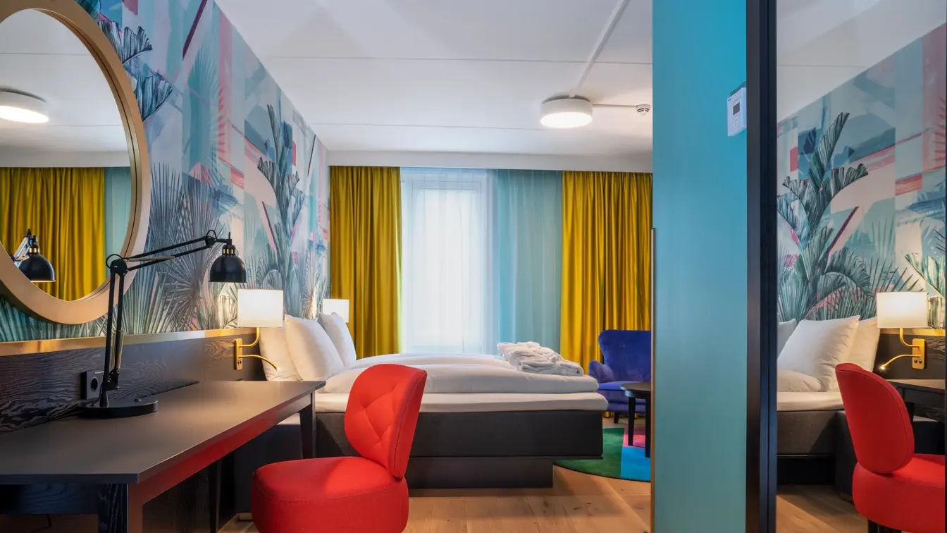 Skrivebord, rød stol, speil og dobbeltseng i superior HCP rom på Thon Hotel Storo