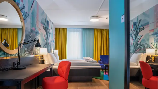 Skrivebord, rød stol, speil og dobbeltseng i superior HCP rom på Thon Hotel Storo