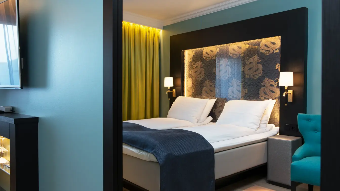 Dobbeltseng blå lenestol, gule gardiner og dragemlnster på seng på Thon hotel Terminus i Oslo sentrum nær Jernbanetorget