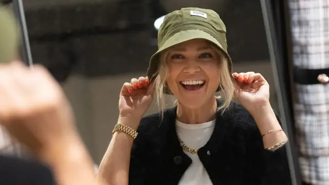 Ung kvinne som smiler mot et speil mens hun drar en grønn fiskehatt ned over hodet