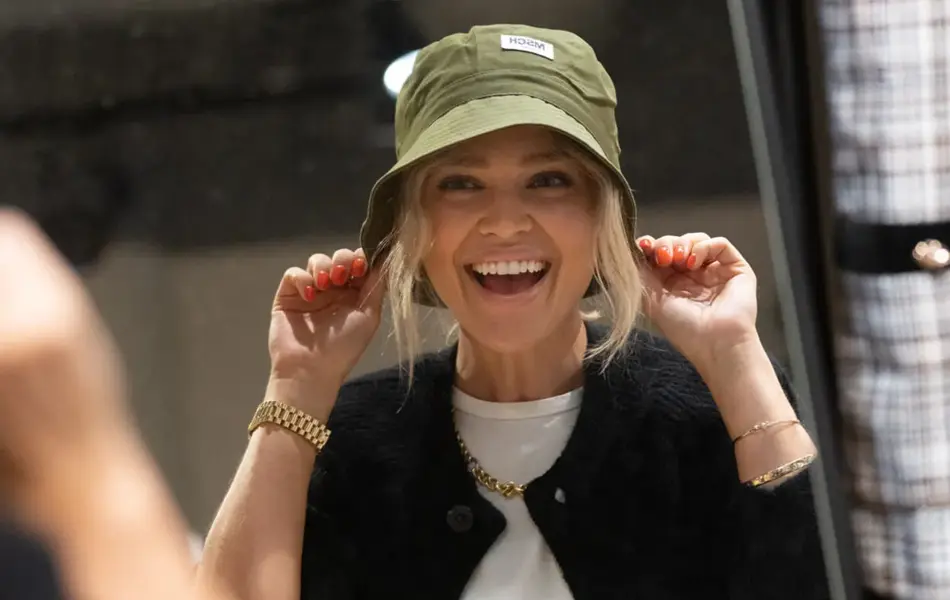 Ung kvinne som smiler mot et speil mens hun drar en grønn fiskehatt ned over hodet