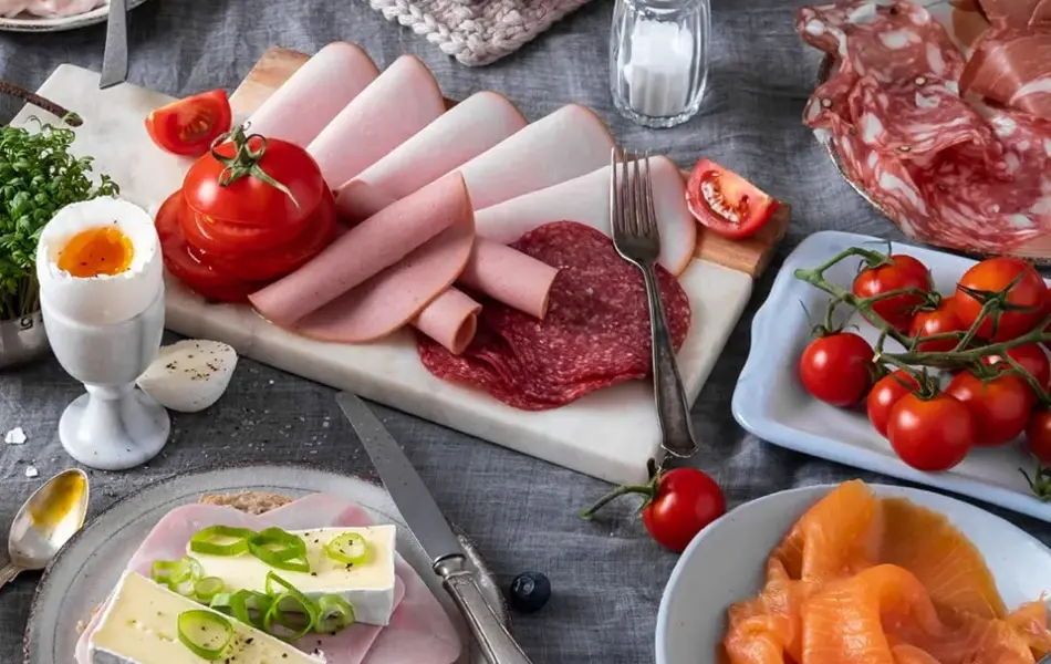 Bord dekket med pålegg - skinke, ost, laks, egg, tomater og boller