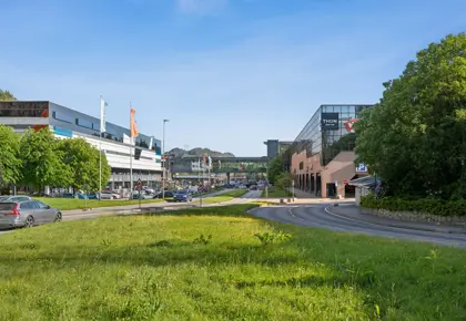 Eksteriørbilde av Thon Senter Vestkanten med kontor- og handelsbygg, gangbro mellom bygninger og grøntområde langs veien.