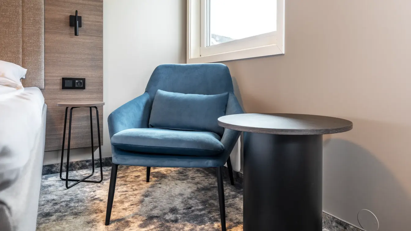 Detaljbilde av standard rom med nattbord, og lenestol 