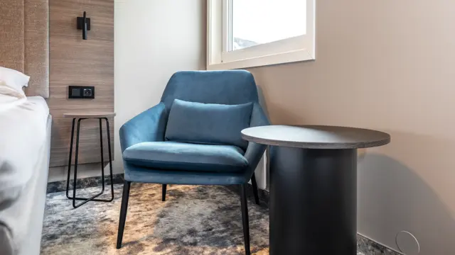 Detaljbilde av standard rom med nattbord, og lenestol 