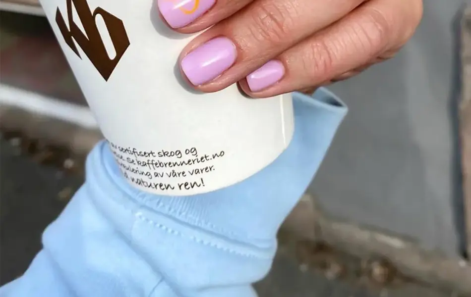 Dame som holder en take away kopp og har nye lakkerte negler