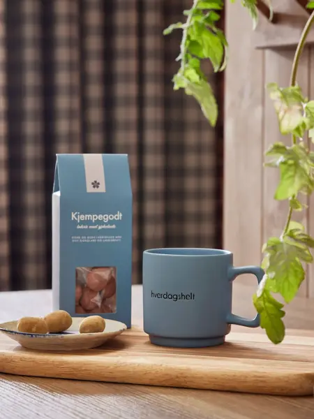 blått krus står på en trefjøl sammen med en pose godis.