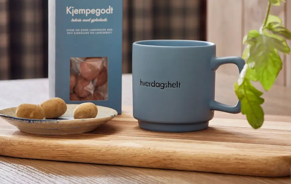 blått krus står på en trefjøl sammen med en pose godis.