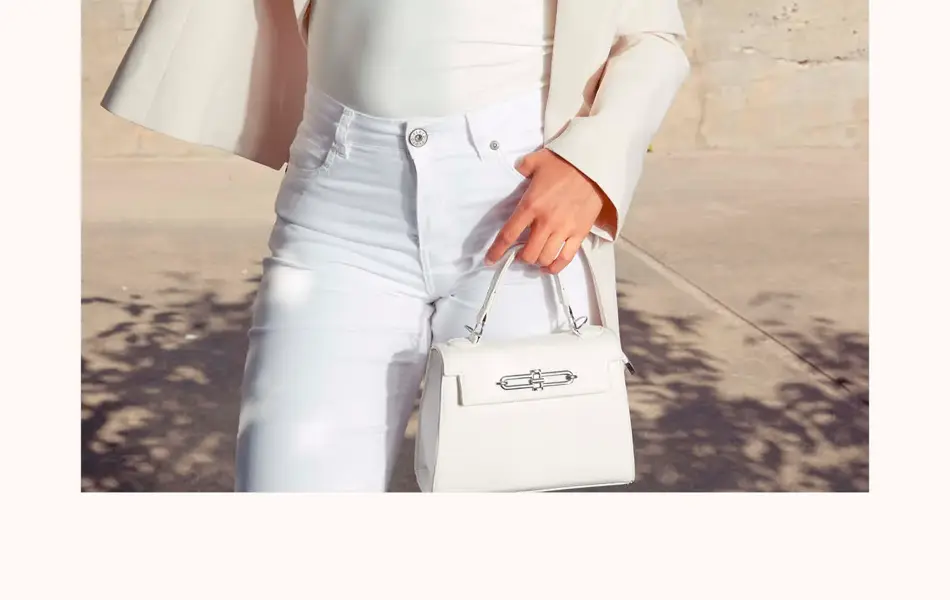 Dame står ute med hvit dressjakke, hvit singlet, hvite jeans og liten hvit veske.