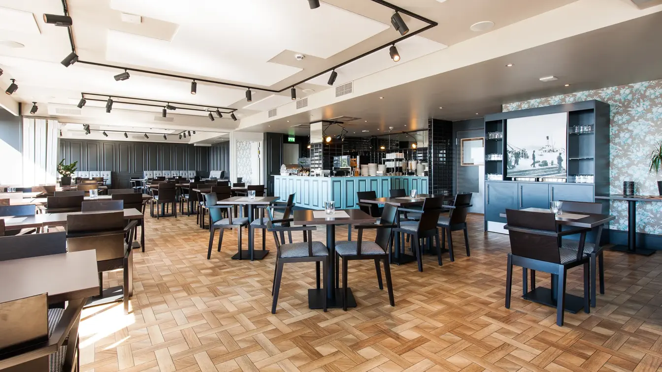 Spiseområde, brune bord og stoler, vindu, hvitt tak, lyse vegger.