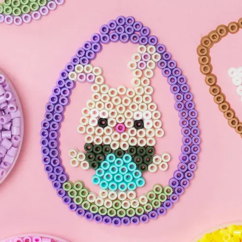 Næriblde av et perlet påskeegg med en kanin som ligger på en rosa duk.