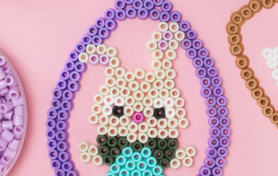 Næriblde av et perlet påskeegg med en kanin som ligger på en rosa duk.