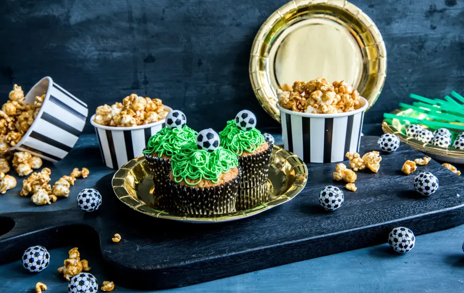 Bord med fotballcupcakes på gulltallerkener og popcorn i skåler 