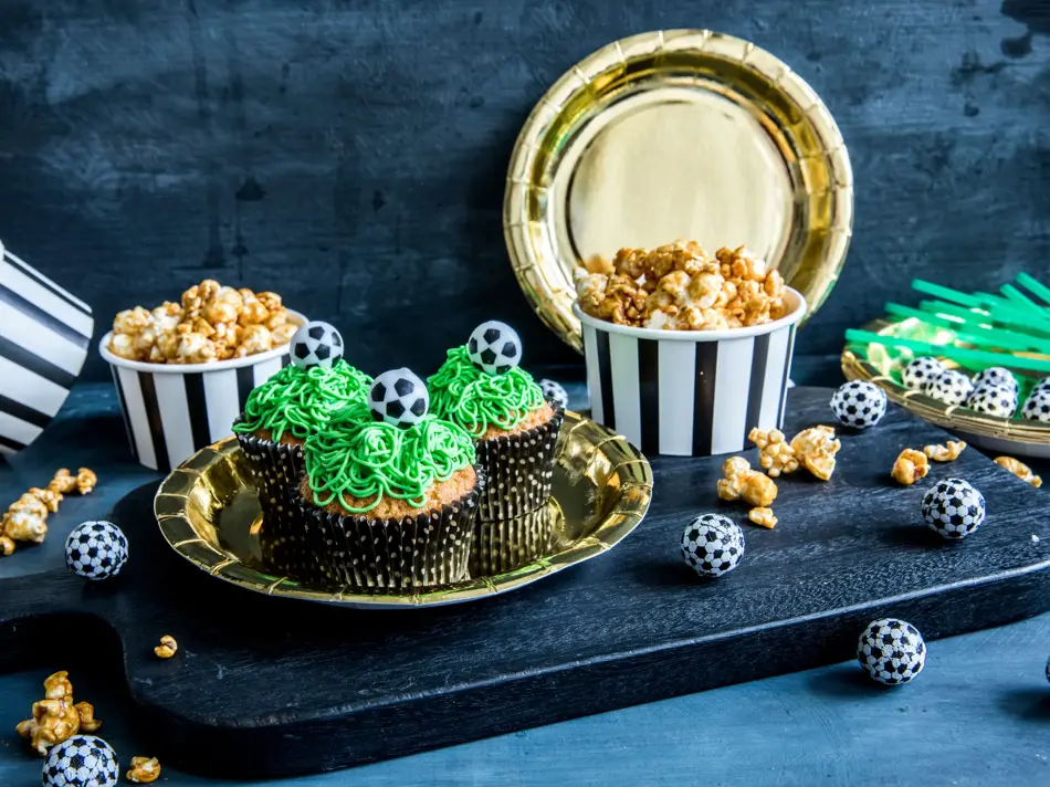 Bord med fotballcupcakes på gulltallerkener og popcorn i skåler 