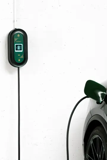 Del av en mørk bil står i en garasje med en ladekabel bak på en hvit vegg.
