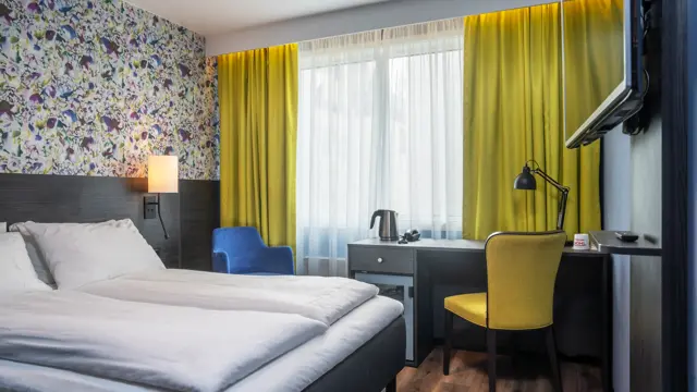Gule gardiner, parkettgulv, gul stol, blomstertapet vegg, vindu, skrivebordpult, TV, dobbeltseng