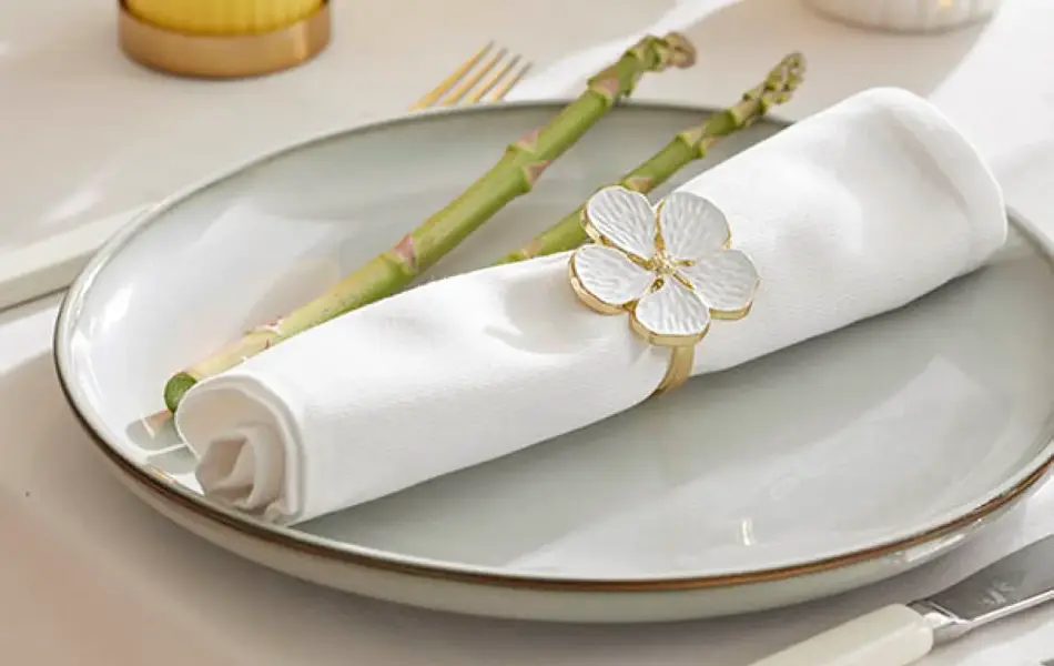 Kuvert på bord med hvit duk, gult kubbelys, pynteegg, blomst, tallerken med hvit serviett og serviettring.