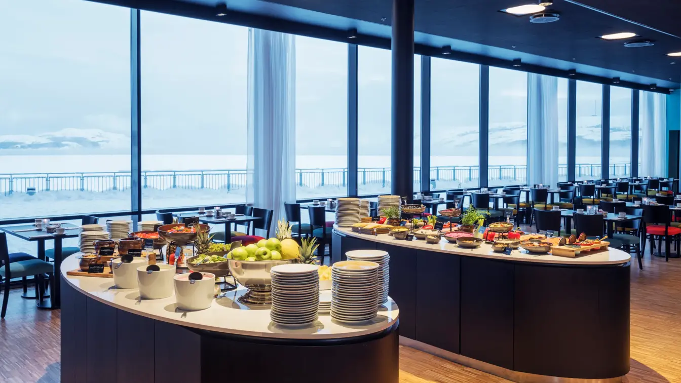 Frokostbuffet og spisebord med store vinduer som gir utsikt mot kaia og havet på Thon Hotel Kirkenes ved kaia i Kirkenes sentrum
