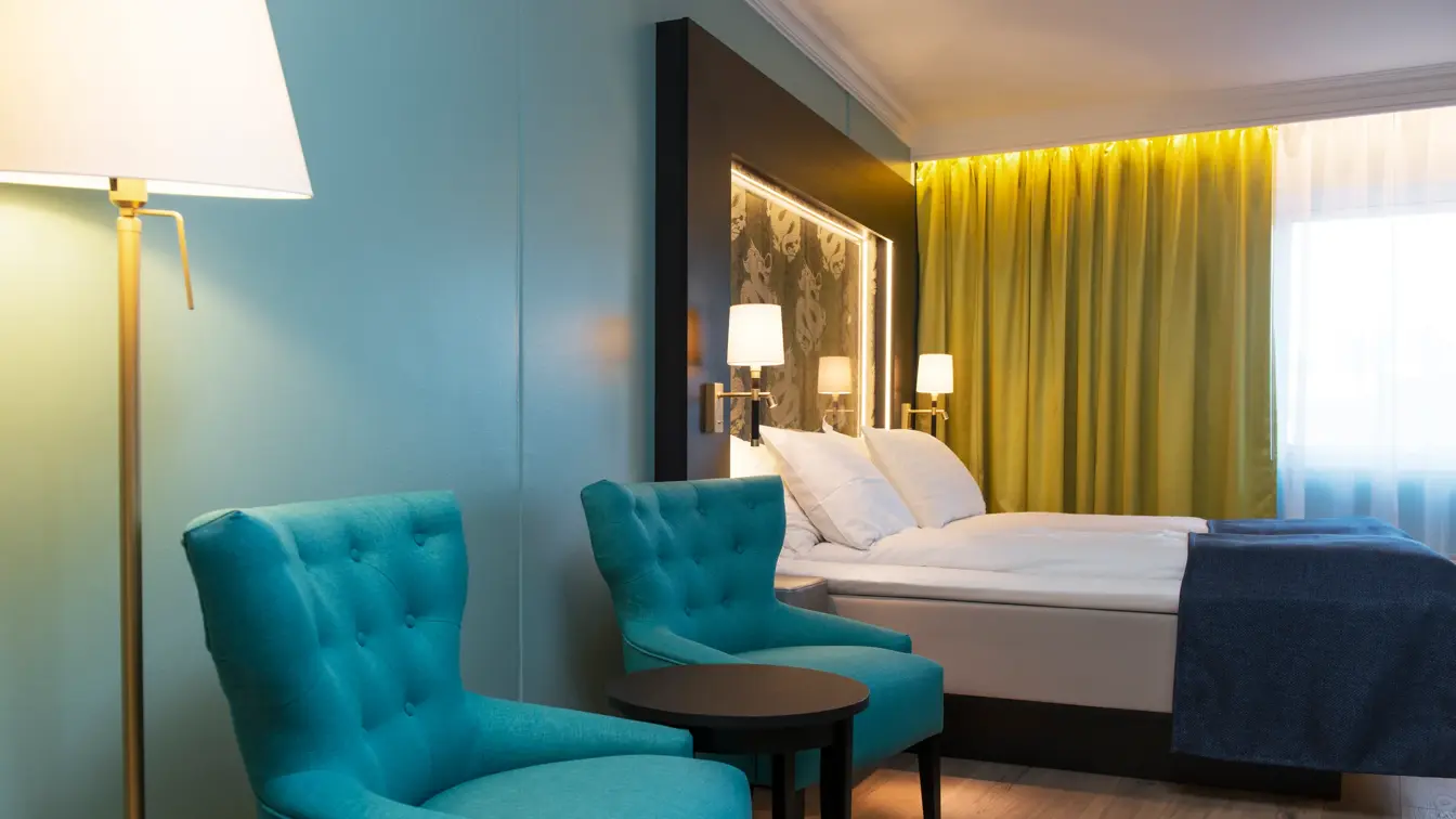 Dobbeltseng blå lenestol, gule gardiner og dragemlnster på seng på Thon hotel Terminus i Oslo sentrum nær Jernbanetorget