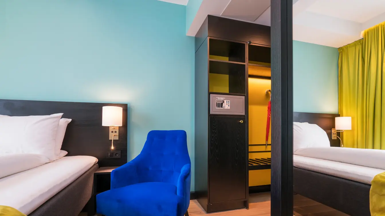 Speil garderobeskap og seng med lenestol ved siden av i dobbeltrom på Thon Hotel Europa i Oslo sentrum rett ved Slottsparken