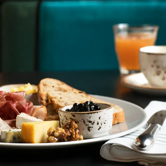 Frokosttallerken med ulike oster, syltetøy, nøtter, spekemat, knekkebrød og brødskive.