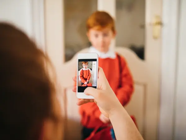 Little boy dressed for his first day back to school, having his photo taken by his Mother on her smartphone.