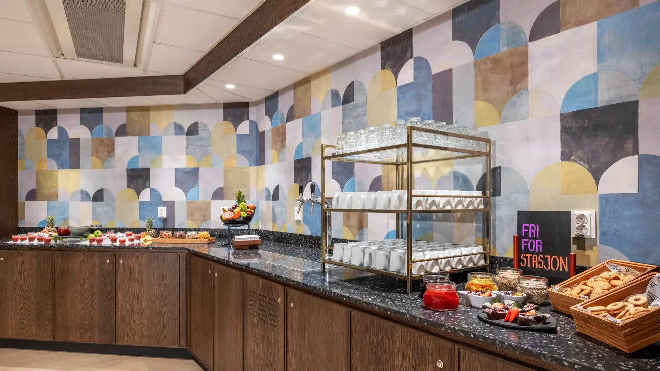 Pausebuffet med diverse bakst, frukt og fargerike smoothies. Mønstret tapet på veggen.