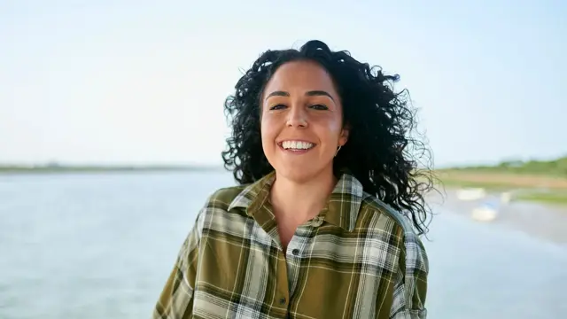 Dame med grønn flanellskjorte smiler i kamera 