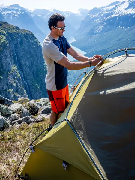 En som setter opp et telt på et fjell med utsikt i bakgrunn