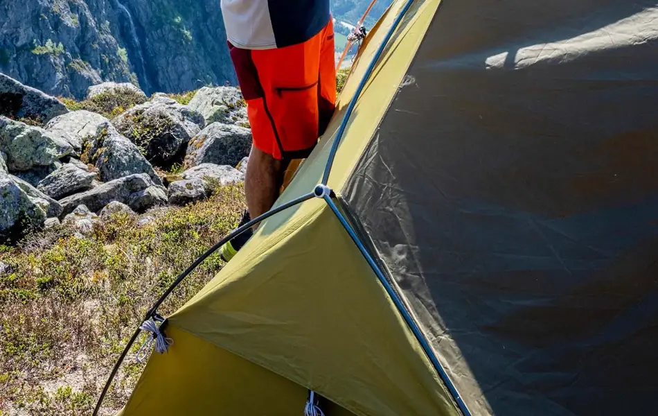 En som setter opp et telt på et fjell med utsikt i bakgrunn