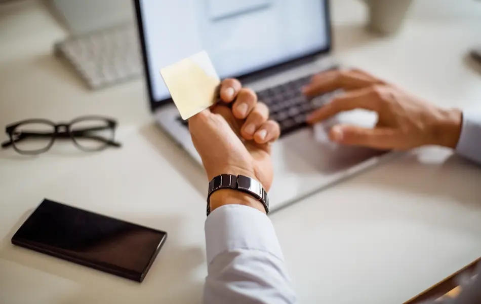 Close up of a man shopping online using laptop with credit card. Man sitting at his desk doing online payment with credit card and laptop.