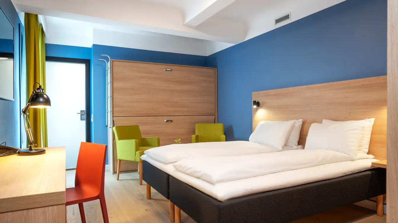 Skrivebord, TV, skap køyeseng, to gule stoler med lite bord og dobbeltseng på familierom på Thon Hotel Astoria