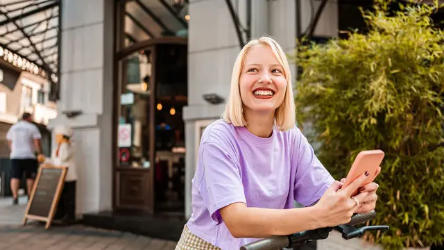 Jente i lys lilla t-skjorte lener seg på sparkesykkel 
