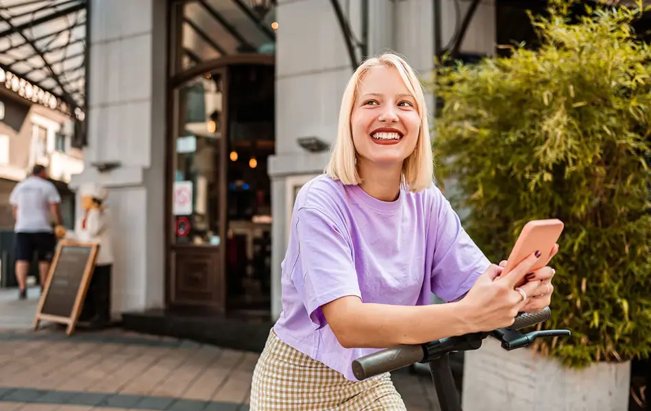 Jente i lys lilla t-skjorte lener seg på sparkesykkel 