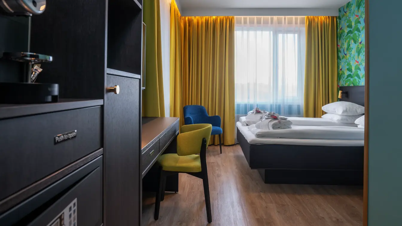 Grønn tapetvegg med mønster, gule gardiner, dobbeltseng, parkettgulv, blå stol, skrivebord, vindu, gul stol