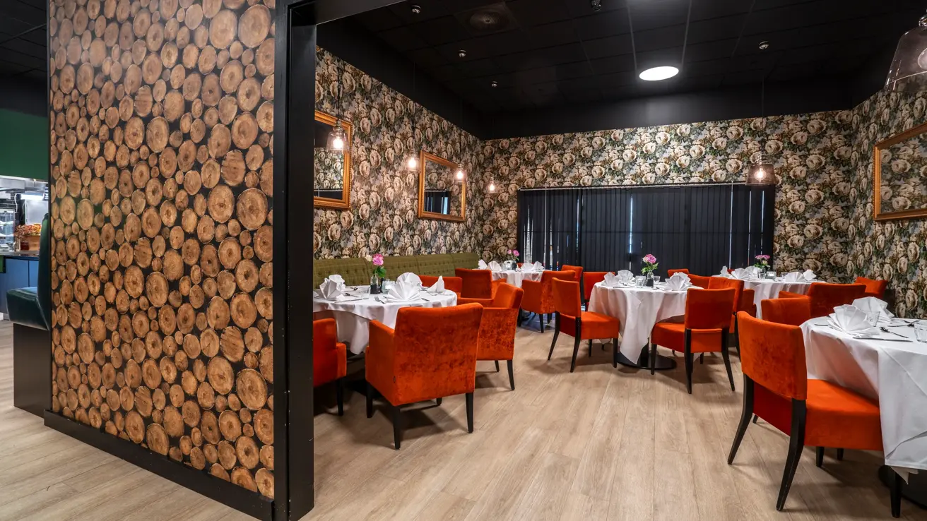 Chambre Separee i restaurant, med runde bord, hvite duker, oransje stoler, og mønstrete tapet.