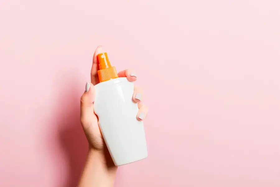 Hånd som holder solkrem med rosa bakgrunn