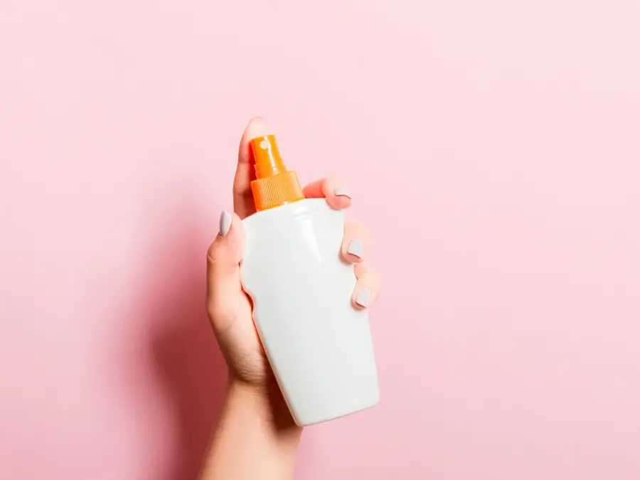 Hånd som holder solkrem med rosa bakgrunn