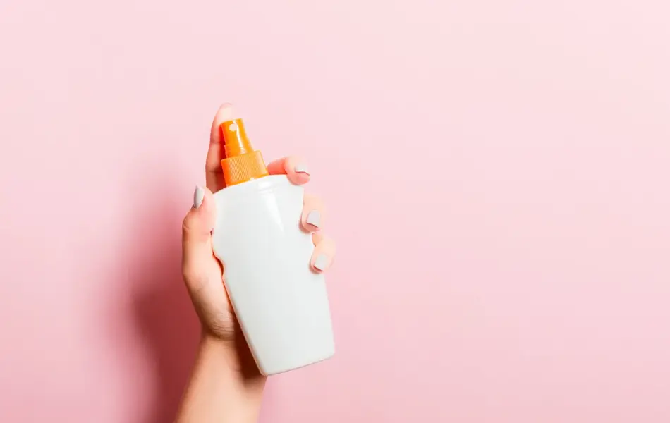 Hånd som holder solkrem med rosa bakgrunn