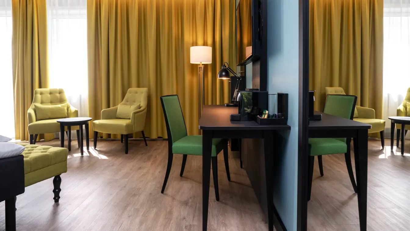 Gule gardiner, to gule lenestoler, salongbord, skrivebord, grønn stol, TV, vindu, gule gardiner, veggspeil.